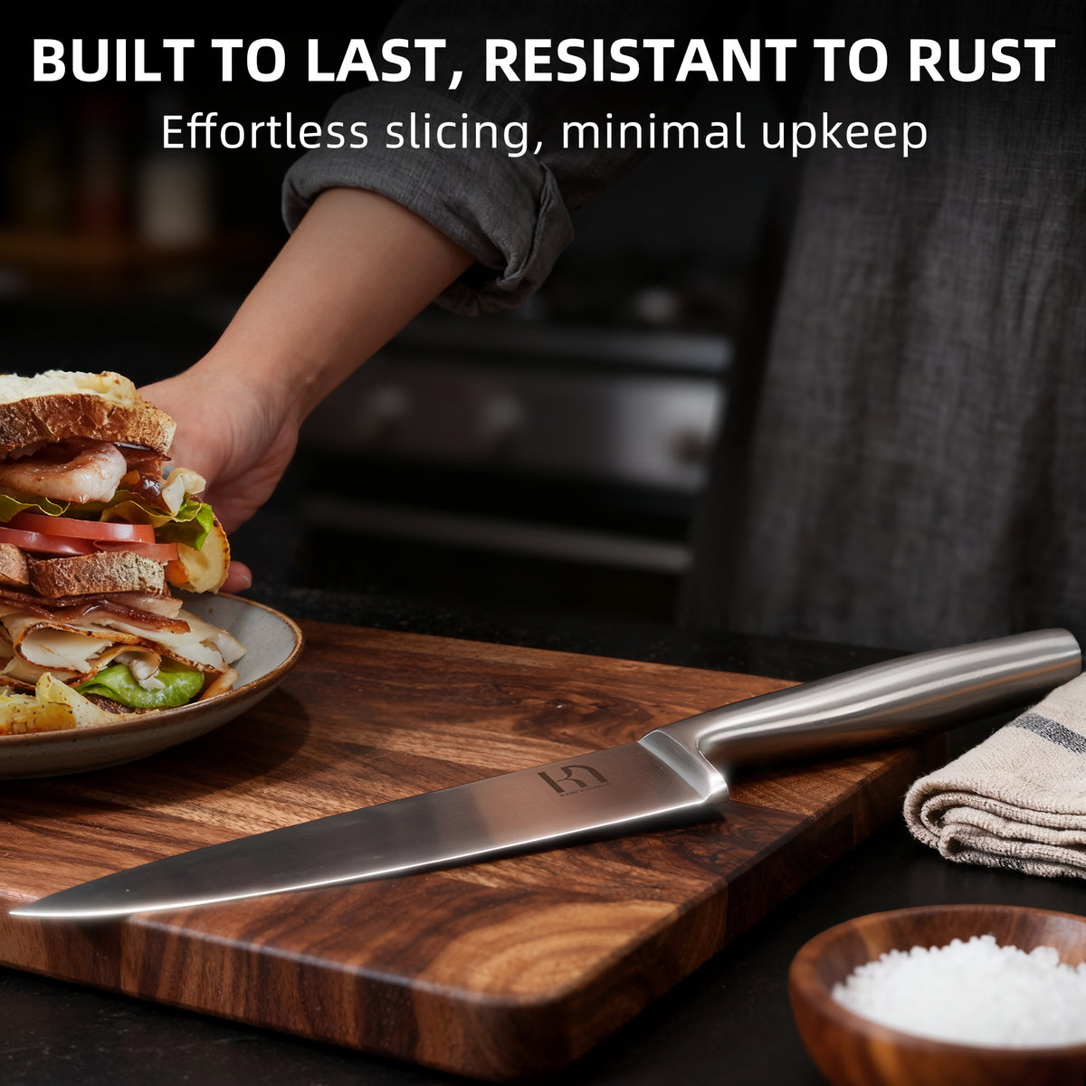 KnifeSaga chef knife resting on wooden cutting board next to a freshly made sandwich, showing rust-resistant low-maintenance stainless steel blade for everyday kitchen use
